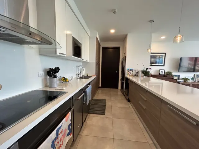 Modern kitchen with white countertops, stainless steel appliances, upper white cabinets, and lower wooden cabinets.