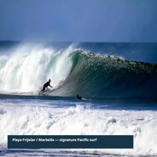 A large ocean wave breaks with white foam, showing a surfer on a board and another person in the water.