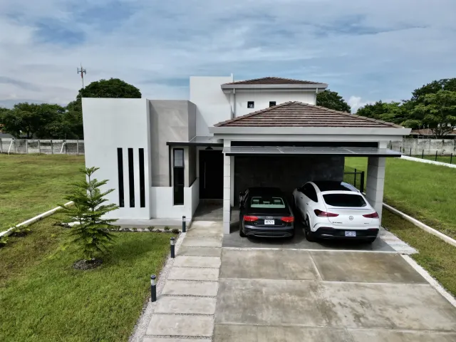 Front view of a two-story modern house with white and gray exterior walls, a tiled roof carport, and two parked cars.