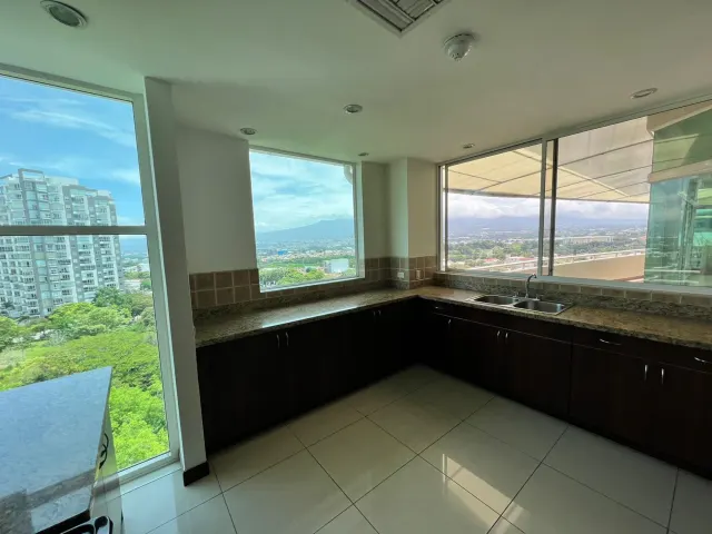 Kitchen area featuring dark lower cabinets, granite countertops, a double-basin sink, and large windows showing urban views.