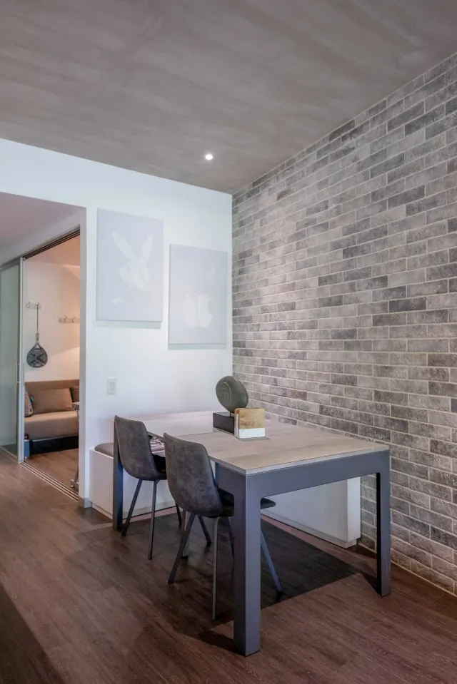 Dining table and chairs set against a textured grey brick accent wall, with a view into an adjacent room with a sofa.