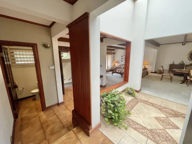 View of an indoor hallway featuring ceramic tile flooring, a half wall with a potted plant, and openings to adjacent living spaces.