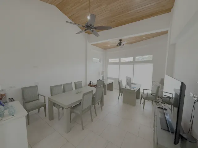 Office room featuring a long table with upholstered chairs, desk setups near large windows, and a sloped wood plank ceiling.