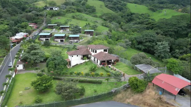 High angle view of multiple buildings surrounded by green hills, trees, and roads.