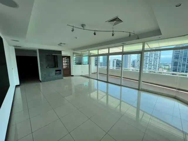 Empty room with light-colored tile flooring, a dark stone feature wall, and floor-to-ceiling glass sliding doors opening to a balcony with city views.