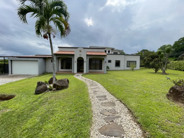 Exterior view of a one-story house featuring a gravel and stone path leading to the entrance, a palm tree on the lawn, and a garage.