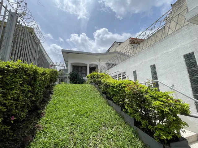 An exterior view showing a sloped grassy walkway bordered by green hedges and a white wall under a partly cloudy sky.