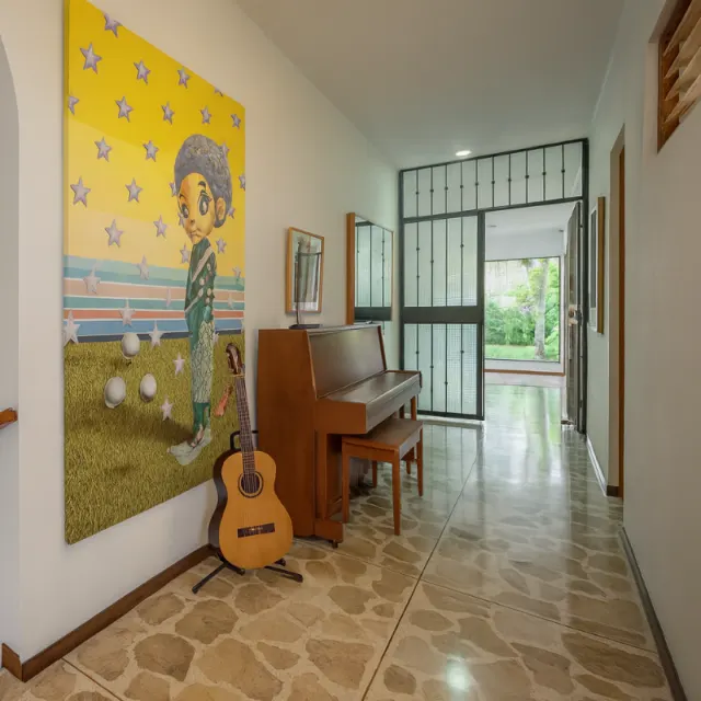 Hallway featuring stone tile flooring, a large yellow painting on the wall, a wooden upright piano with a matching bench, and an acoustic guitar on a stand.