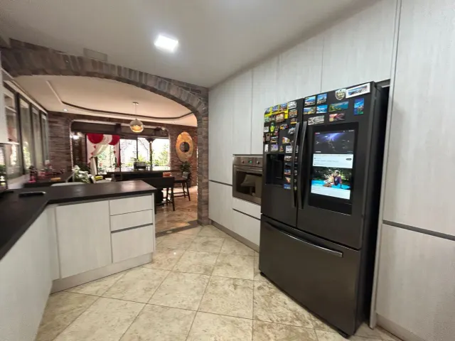 Kitchen featuring light cabinets, tile floors, a built-in oven, and a large black refrigerator with magnets on the door. A brick arch leads to an adjacent dining area.