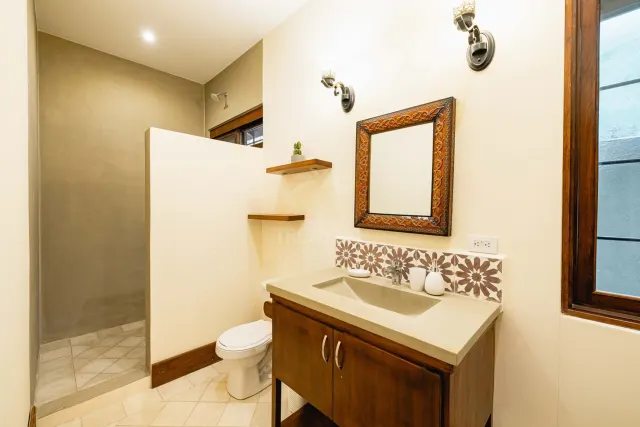 Bathroom featuring a wooden vanity with a concrete sink, a decorative mirror, and a tiled shower area separated by a partial wall.